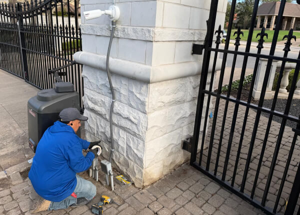 Technician installing security camera wiring at gated community entrance